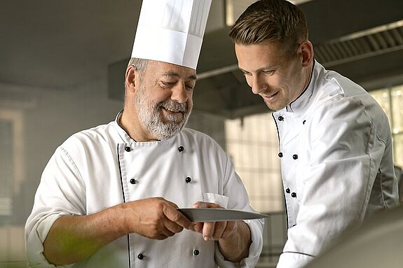 Respekt Ein alter Koch zeigt einem jungen Koch etwas.