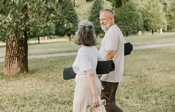 Patienten Outdoor Gymnastik Ein Mann und eine Frau laufen mit Gymnastikmatten auf einer Wiese.