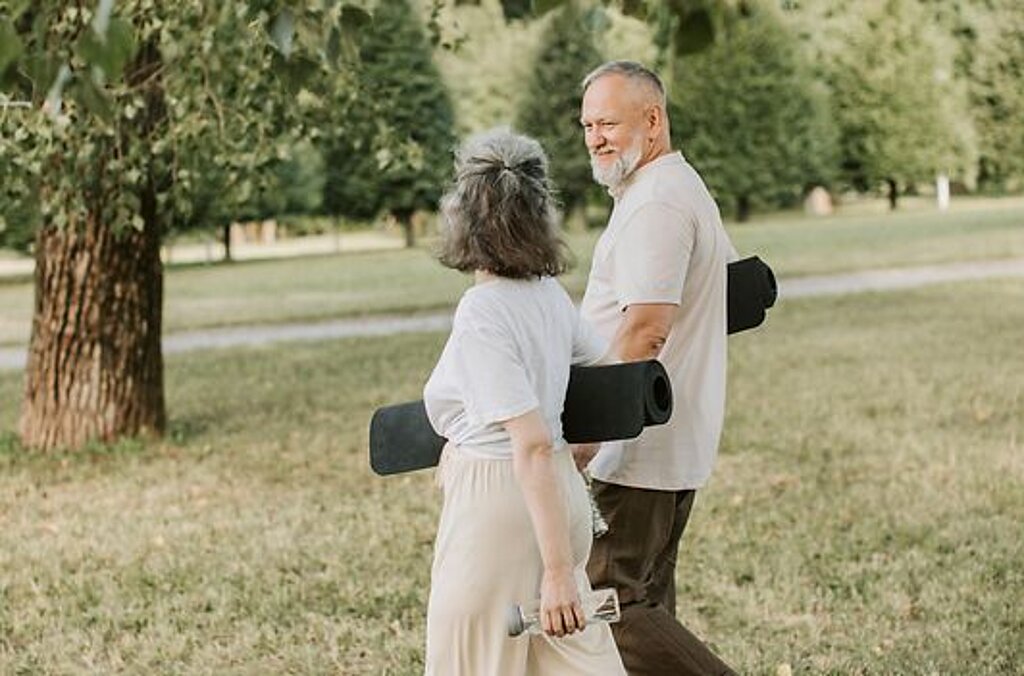 Patienten Outdoor Gymnastik Ein Mann und eine Frau laufen mit Gymnastikmatten auf einer Wiese.