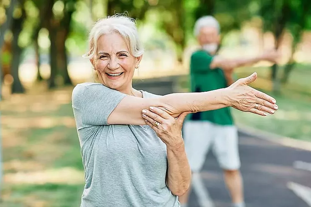 Gymnastik im Park Eine freundlich lächelnde Frau macht Dehnungsübungen im Park.