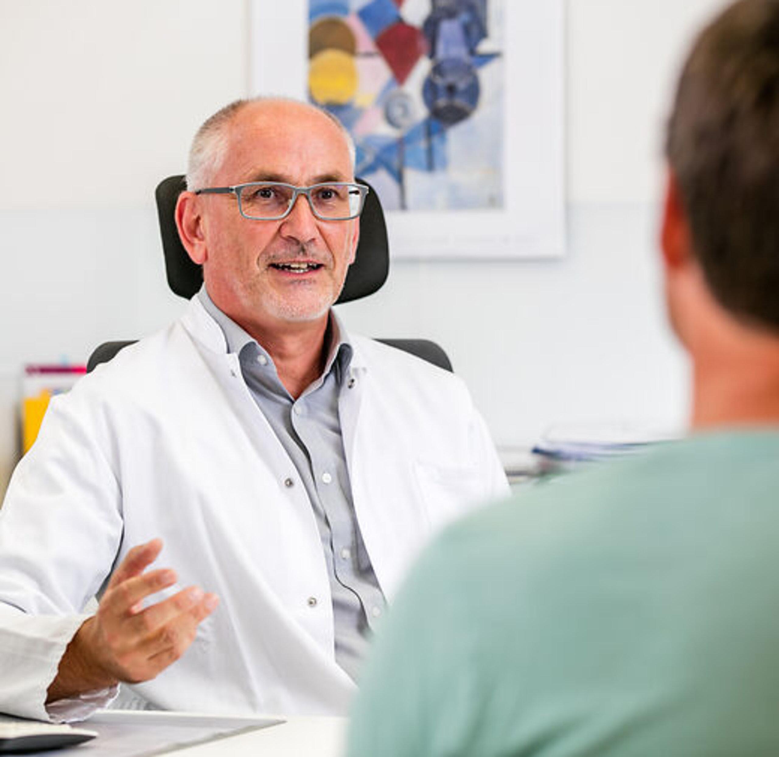 Artgespräch mit Patient Ein Arzt unterhält sich freundlich mit einem Pateinten am Schreibtisch.