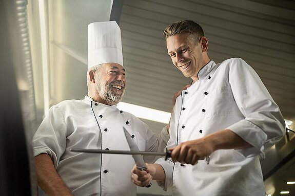 Respekt Ein alter Koch zeigt einem jungen Koch etwas.