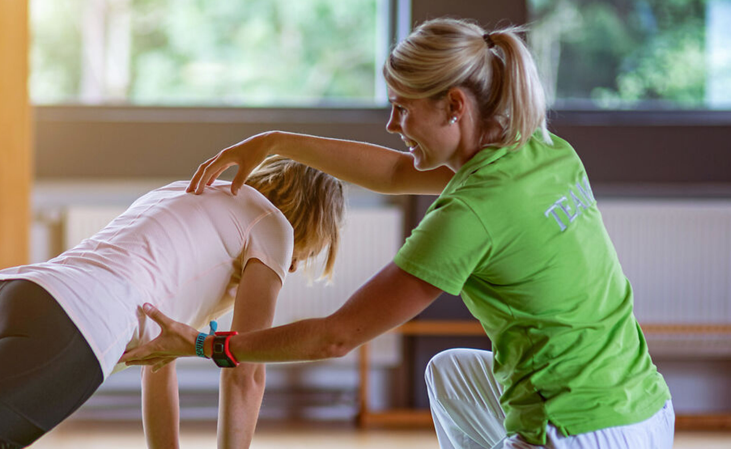 Physiotherapie mit Ball Eine Physiotherapeutin unterstützt eine junge Patientin bei einer Stützübung auf einem Ball.