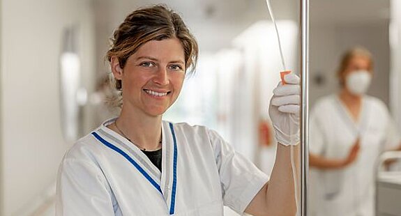 Pflege Infusion Eine Pflegerin steht mit einem Infusionsgerät im Gang einer Klinik.