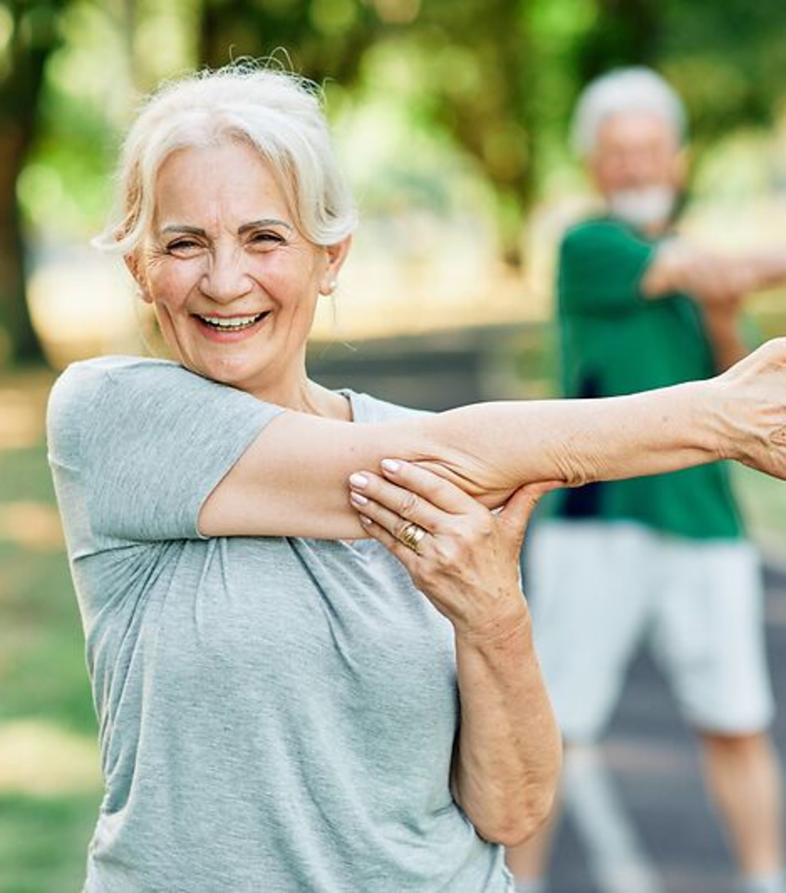 Patientin Gymnastik im Park Frau macht Arm-Dehnübungen im Park und lächelt dabei freundlich.