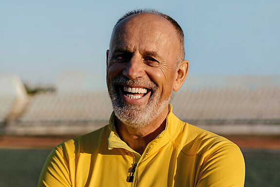 Mann lachend Ein Mann im Rentenalter lacht freundlich im Fußballstadion.