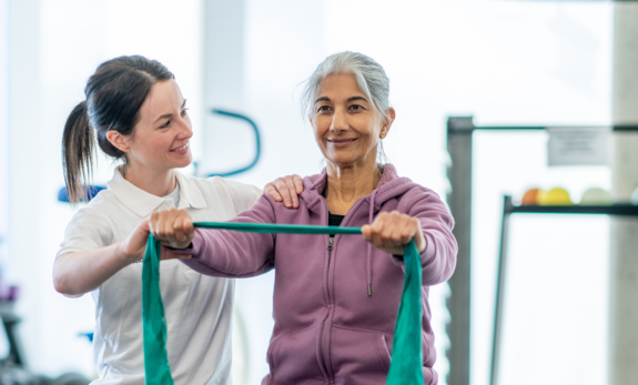 Physiotherapie mit Ball Eine Therapeutin unterstützt eine Patientin bei Übungen mit dem Therraband.
