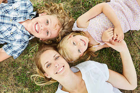 Mutter mit Kindern Eine Mutter liegt mit zwei Kindern auf einer Wiese.