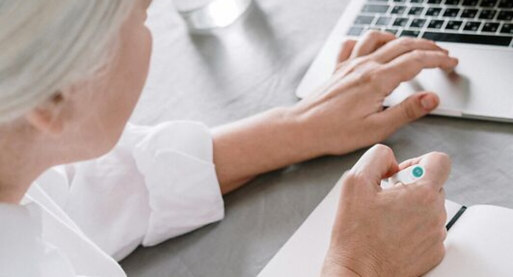 Frau recherchiert am Laptop Eine ältere Frau sucht etwas am Laptop und macht sich dabei Notizen auf einen Block.