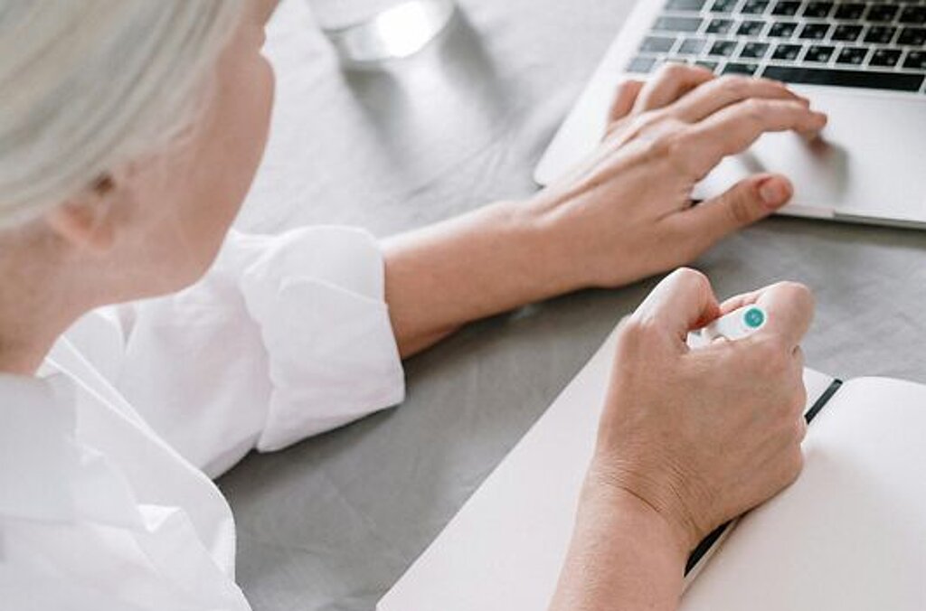 Frau am Laptop Eine ältere Frau sucht etwas am Laptop und macht sich dabei Notizen auf einen Block.