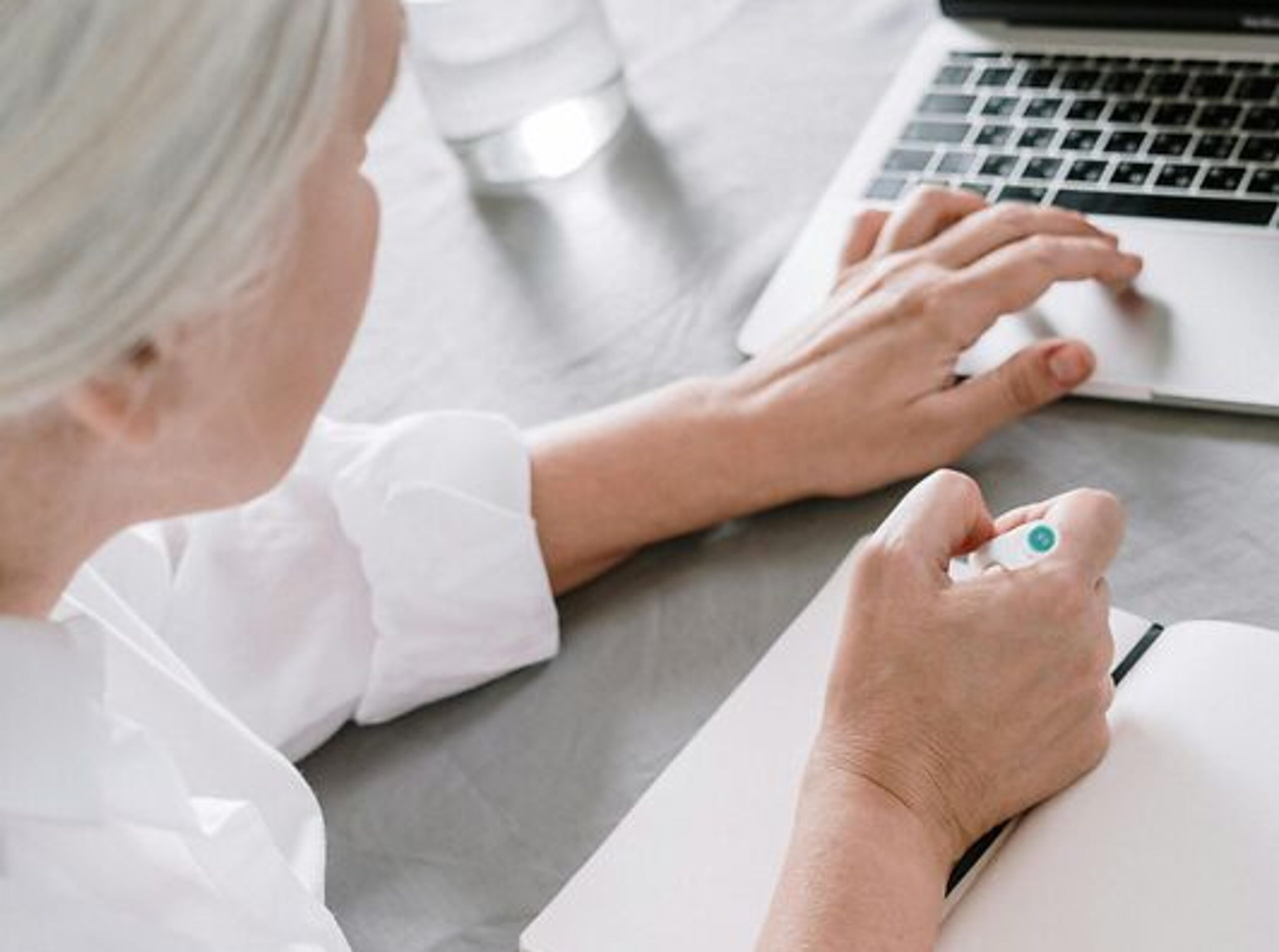 Frau am Laptop Eine ältere Frau sucht etwas am Laptop und macht sich dabei Notizen auf einen Block.