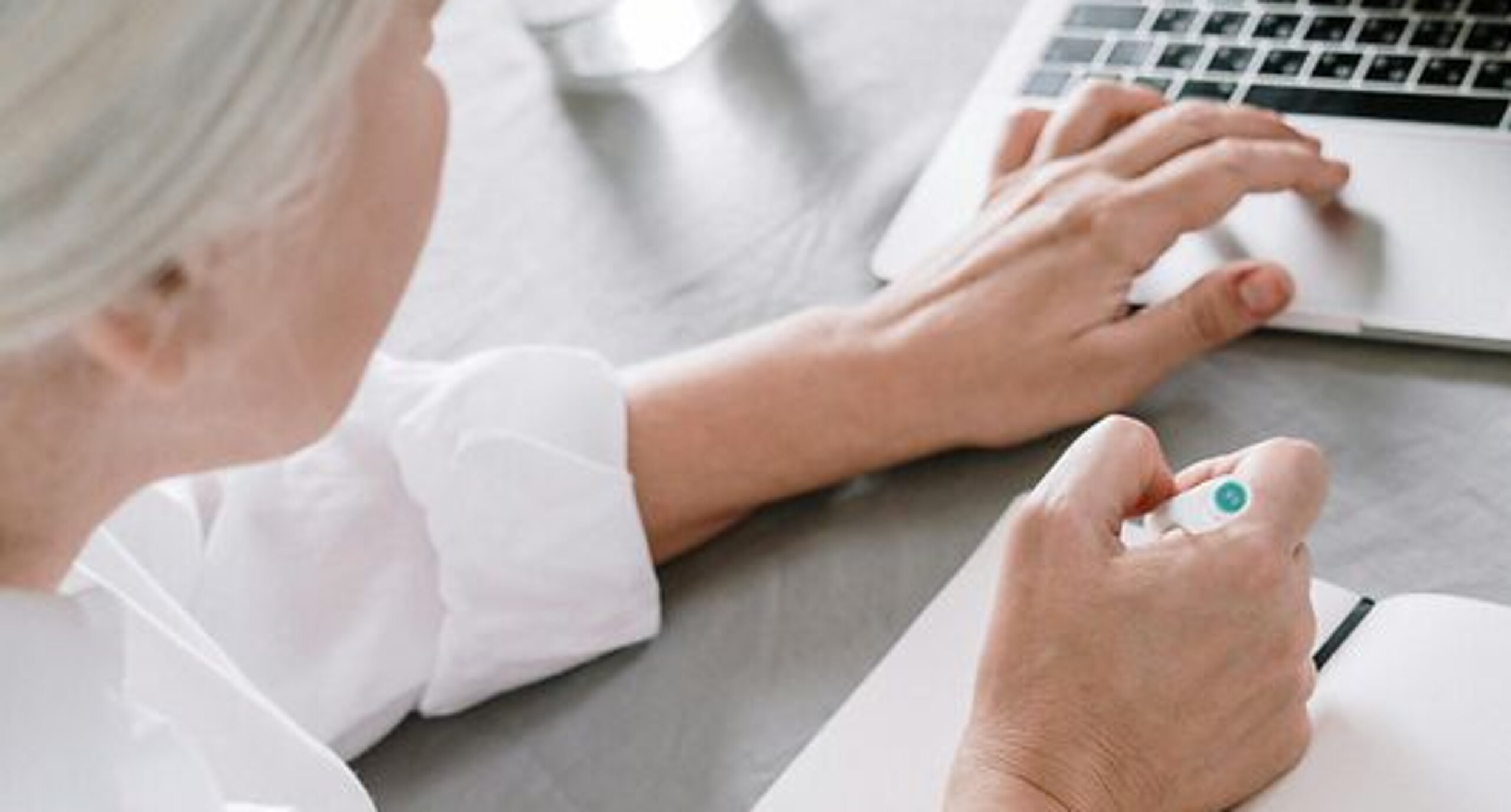 Frau am Laptop Eine ältere Frau sucht etwas am Laptop und macht sich dabei Notizen auf einen Block.