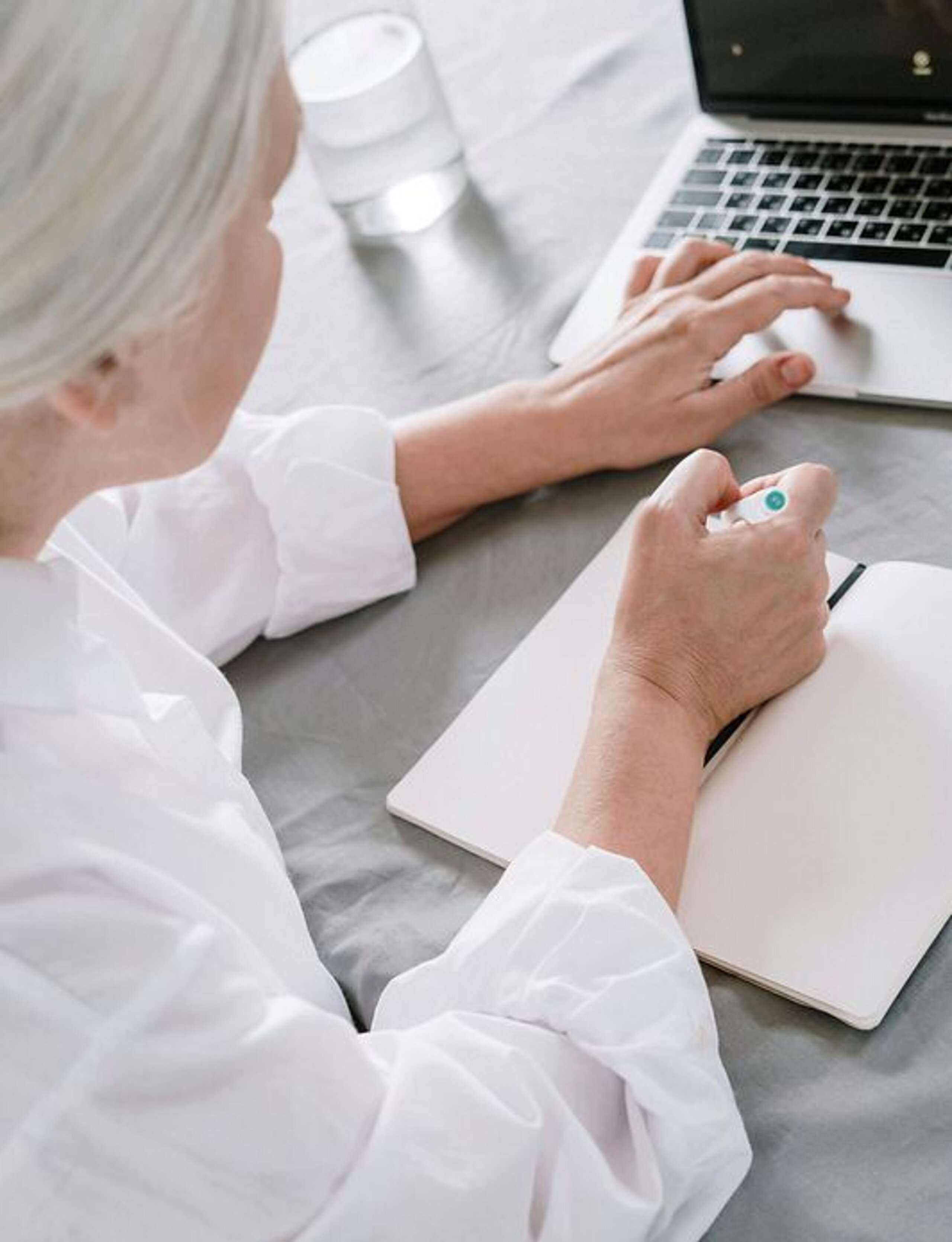 Frau recherchiert am Laptop Eine ältere Frau sucht etwas am Laptop und macht sich dabei Notizen auf einen Block.