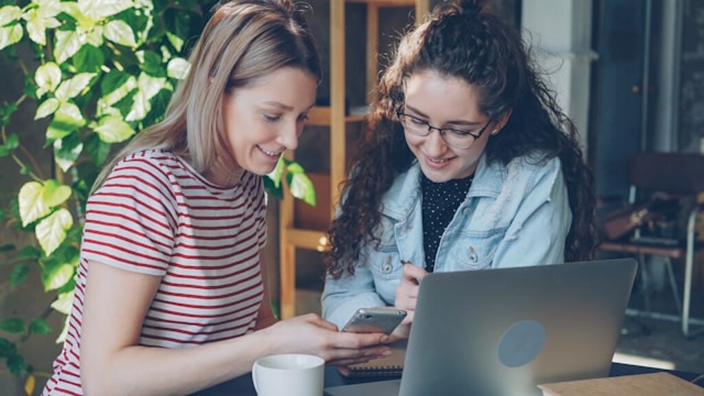 Studentinnen Zwei Studentinnen schauen gemeinsam in einen Laptop und ein Smartphone.