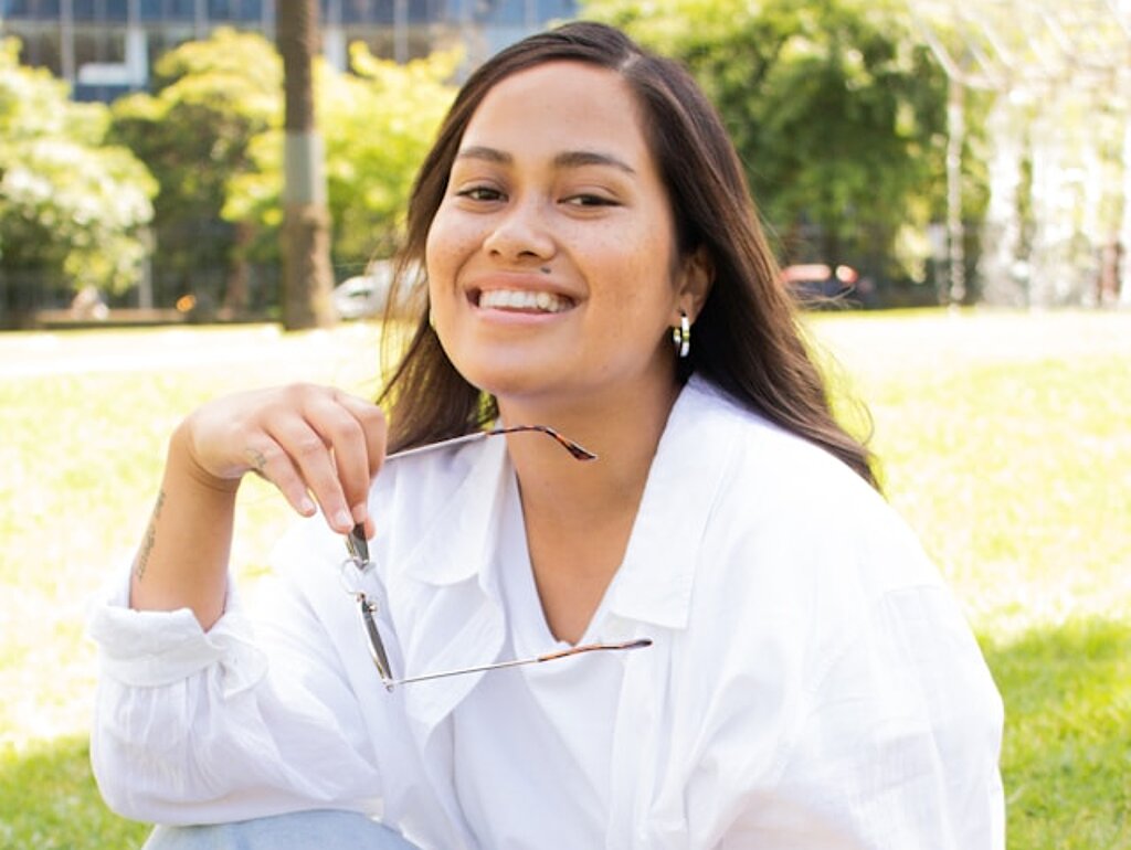 Studentin Park Eine Studentin sitzt lachend im Park mit Tasche.