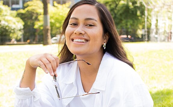 Studentin Park Eine Studentin sitzt lachend im Park mit Tasche.