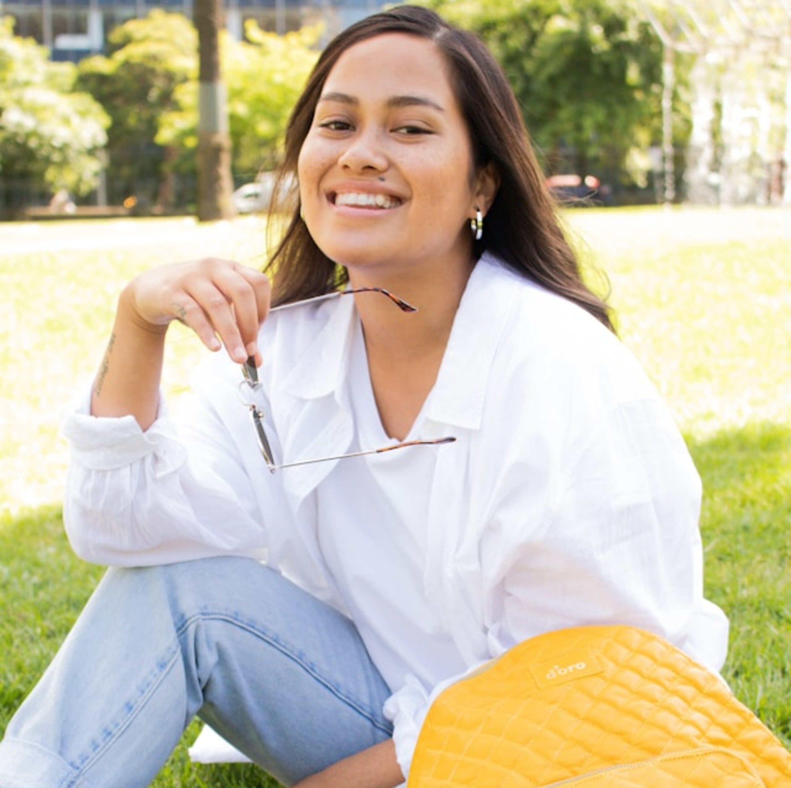 Studentin Park Eine Studentin sitzt lachend im Park mit Tasche.
